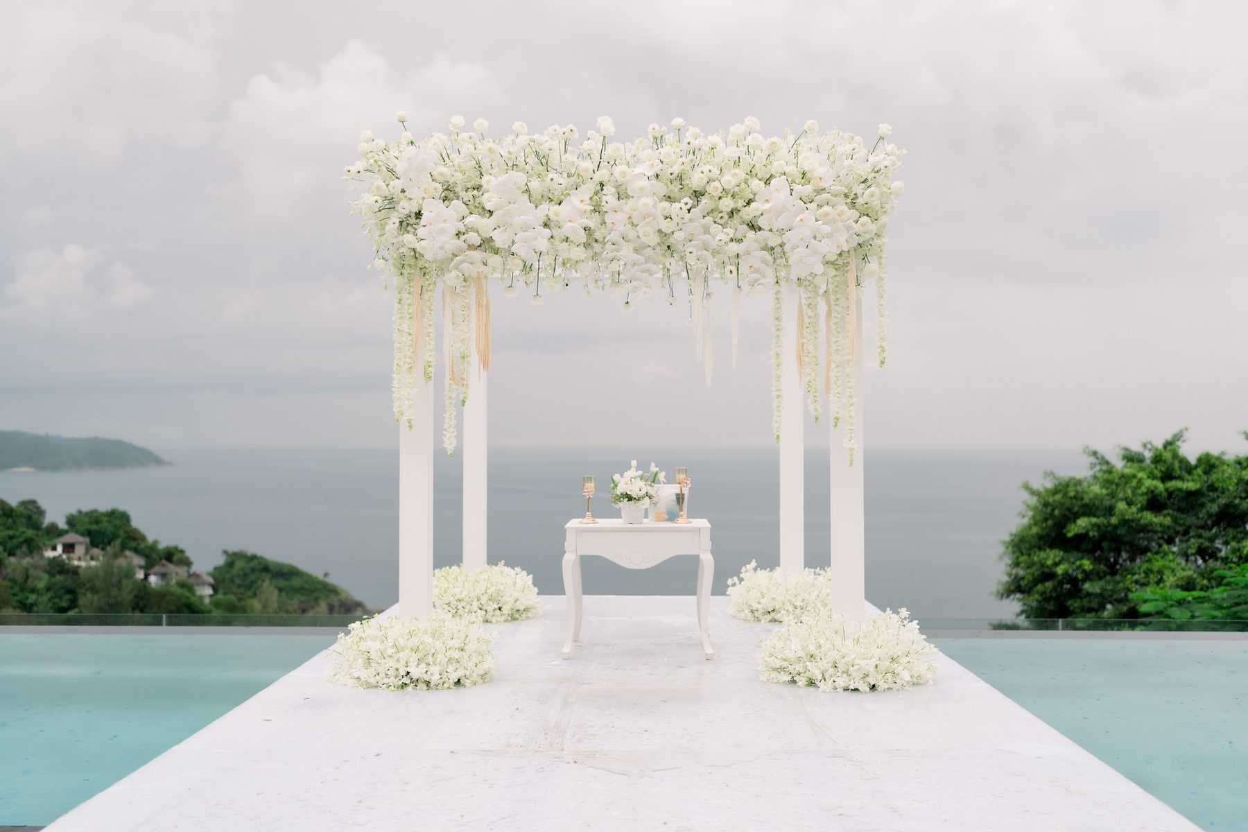 Symmetrical ivory floral pillars framing an infinity-pool ceremony aisle at Villa Aye, by Wedding Flowers Phuket