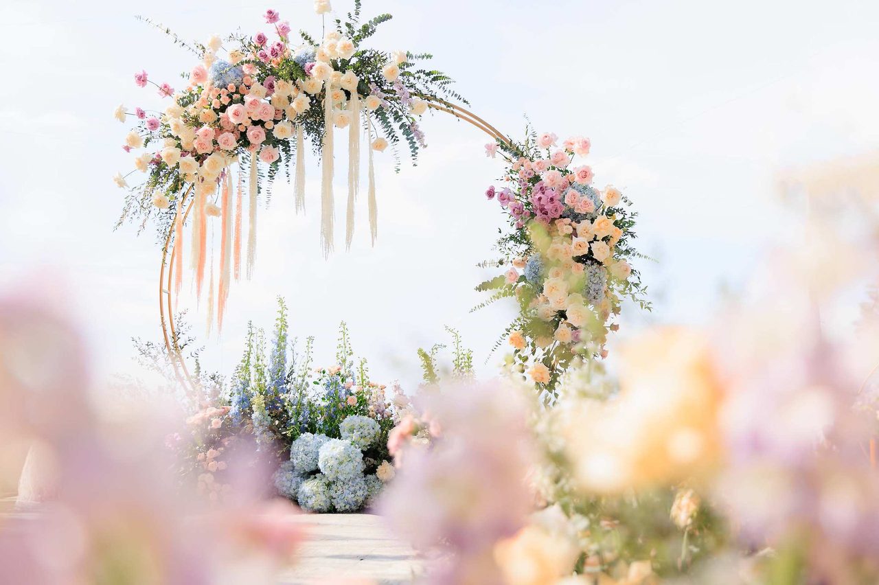 Pastel circular ceremony arch with the villa architecture of Baan Phu Prana behind, by Wedding Flowers Phuket